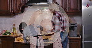 Back view of son helping mother frying healthful vegetables for dinner at home. Brunette Caucasian boy in apron learning