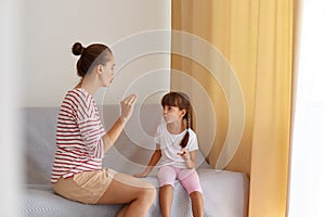 Back view of speech pathologist teaching little kid daughter right sounds pronunciation, physiotherapist working on speech defects