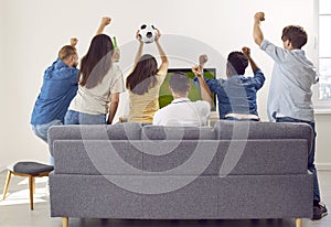 Back view of sport fans sitting on couch watching soccer football match on TV, rejoicing in victory.