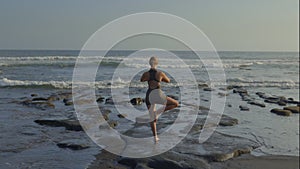 Back View of the Sporty Caucasian Blonde Girl Practicing Vrksasana Pose Outside on the Beach.