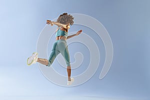 Back view of sporty woman running in Mid-Air exercising during cardio workout over studio background