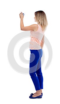 Back view of standing young beautiful woman and using a mobile