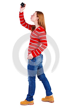 Back view of standing young beautiful woman and using a mobile