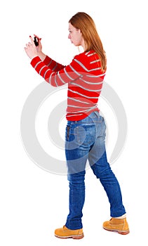 Back view of standing young beautiful woman using a mobile pho