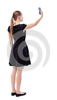 Back view of standing young beautiful woman using a mobile pho