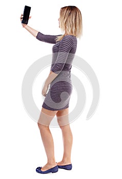 Back view of standing young beautiful woman using a mobile pho