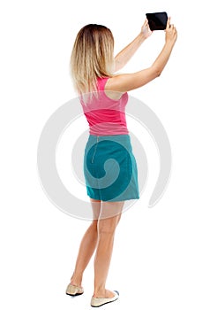 Back view of standing young beautiful woman using a mobile pho