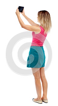 Back view of standing young beautiful woman using a mobile pho