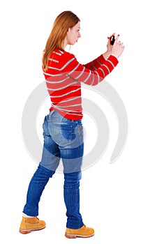 Back view of standing young beautiful woman using a mobile pho