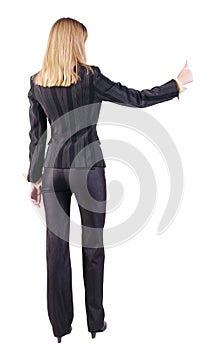 Back view of standing young blonde business woman showing thumb