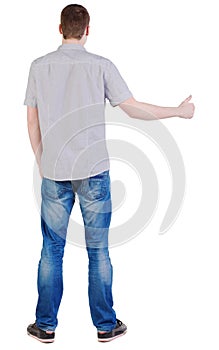 Back view of standing Young brunette man showing thumb up.