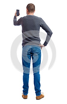 Back view of standing young man and using a mobile phone.