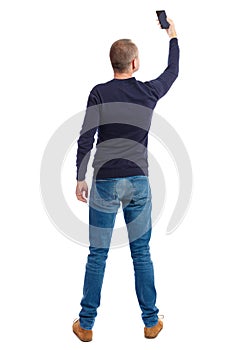 Back view of standing young man and using a mobile phone.