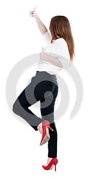 Back view of standing young redhead business woman showing thumb