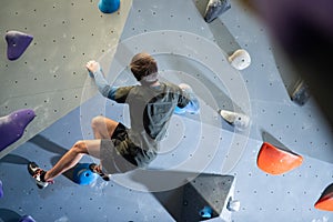 Back view of strong athlete training climbing artificial wall