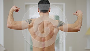 Back view of strong athletic Middle Eastern man raising hands showing strength gesture indoors. Confident muscular