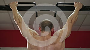 Back view of strong male athlete with muscular arms and shoulders hanging on bar