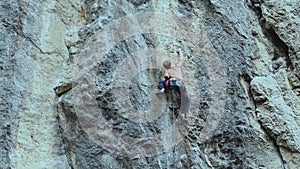 Back view strong muscular man rock climber climbing on sport route outdoors on a vertical cliff