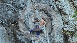 Back view strong muscular man rock climber climbing on sport route outdoors on a vertical cliff