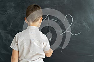 Back view of a student in a class writes chalk numbers on a blackboard. Math lesson. Junior School. Education concept