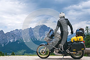 Back view of stylish biker on adventure touring motorcycle in full equipment on dirt road, Look at distance on top of Dolomites