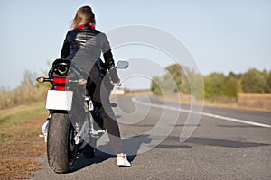Back view of stylish biker on motorbike, covers long destination, rides in countryside in open road, enjoys time for relax, likes