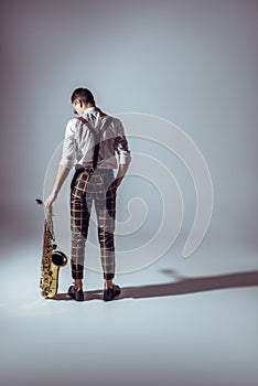 back view of stylish young musician standing with saxophone