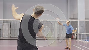 Back view of tattooed Caucasian sportsman competing in badminton with young blurred man at the background. Middle shot