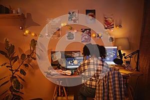 Back view of teen black girl using computer studying at home in night light