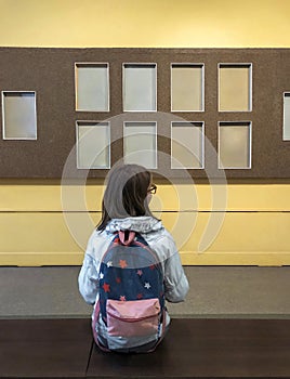 Back view of teen school girl with backpack sitting on bench in museum