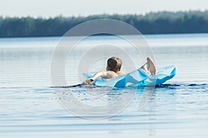 Back view of teenager paddling with his arms and floating on blue pool lilo outdoors