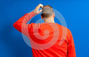 Back view of thoughtful man scratching his head over blue background. He wonders why he doesn& x27;t have luck in life