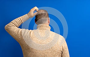 Back view of thoughtful man scratching his head over blue background. He wonders why he doesn't have luck in life