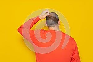 Back view of thoughtful man scratching his head over yellow background. He is doubting his existence, he does not