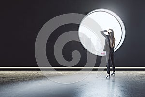 Back view of thoughtful young businesswoman standing in creative modern concrete interior with round window and city view. Mock up
