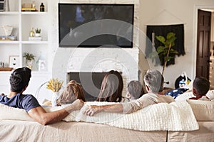 Back view of three generation Hispanic family sitting on the sofa watching TV