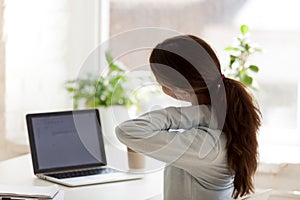 Back view of tired woman touching neck at work desk