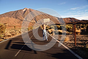 Back view of topless woman walking alone on the empty street in the middle of volcanic landscape, with protest banner