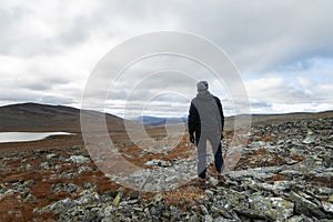 Back view of tourist hiker. Walking on mountain, big rocks on background