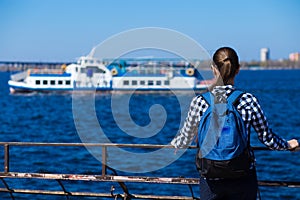 Back view of tourist woman with backpack standing on pier near sea on sunny spring day