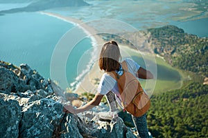 Back view tourist woman climbing up on rock, hiking in mountains over seashore