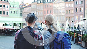 Back view of tourists couple with bags checking map on central city square