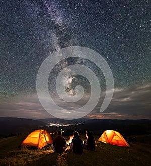 Back view travel team sitting near fire beside camping in night under wonderfull sky with many stars