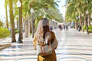 Back view of traveler girl walking on Explanada de Espana promenade of Alicante in the morning. Young female backpacker visiting photo