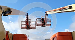 Back view of two aerial work platforms against blue sky with clouds.