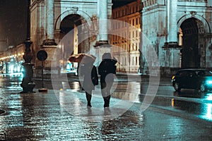 Back view of two female friends walking on the sidewalk under the rain in Munich, Germany