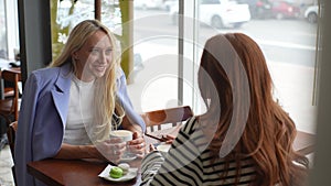 Back view of two happy charming Caucasian female friends talking laughing at cafe table drinking coffee having fun