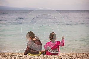 Back view of two little girls sitting near the sea