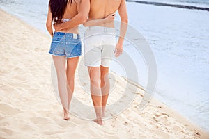 Back view of two lovers walking on the seaside and hugging. Legs on sand