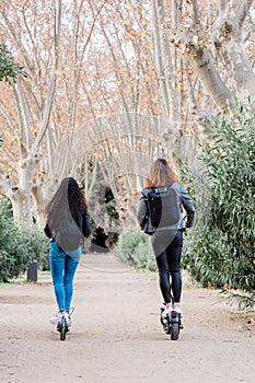 Back view of two multiethnic female friends on electric scooters. Urban lifestyle and ecological transport concepts